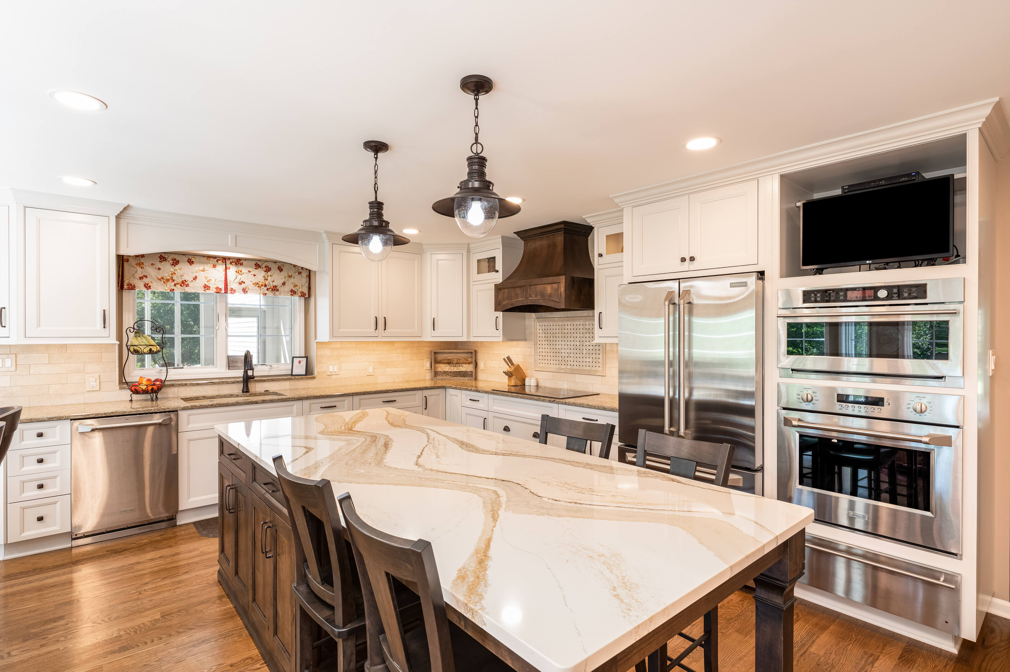 Kitchen with cherry cabinetry, including glass-front display cabinets, stainless steel refrigerator and dual wall ovens. 