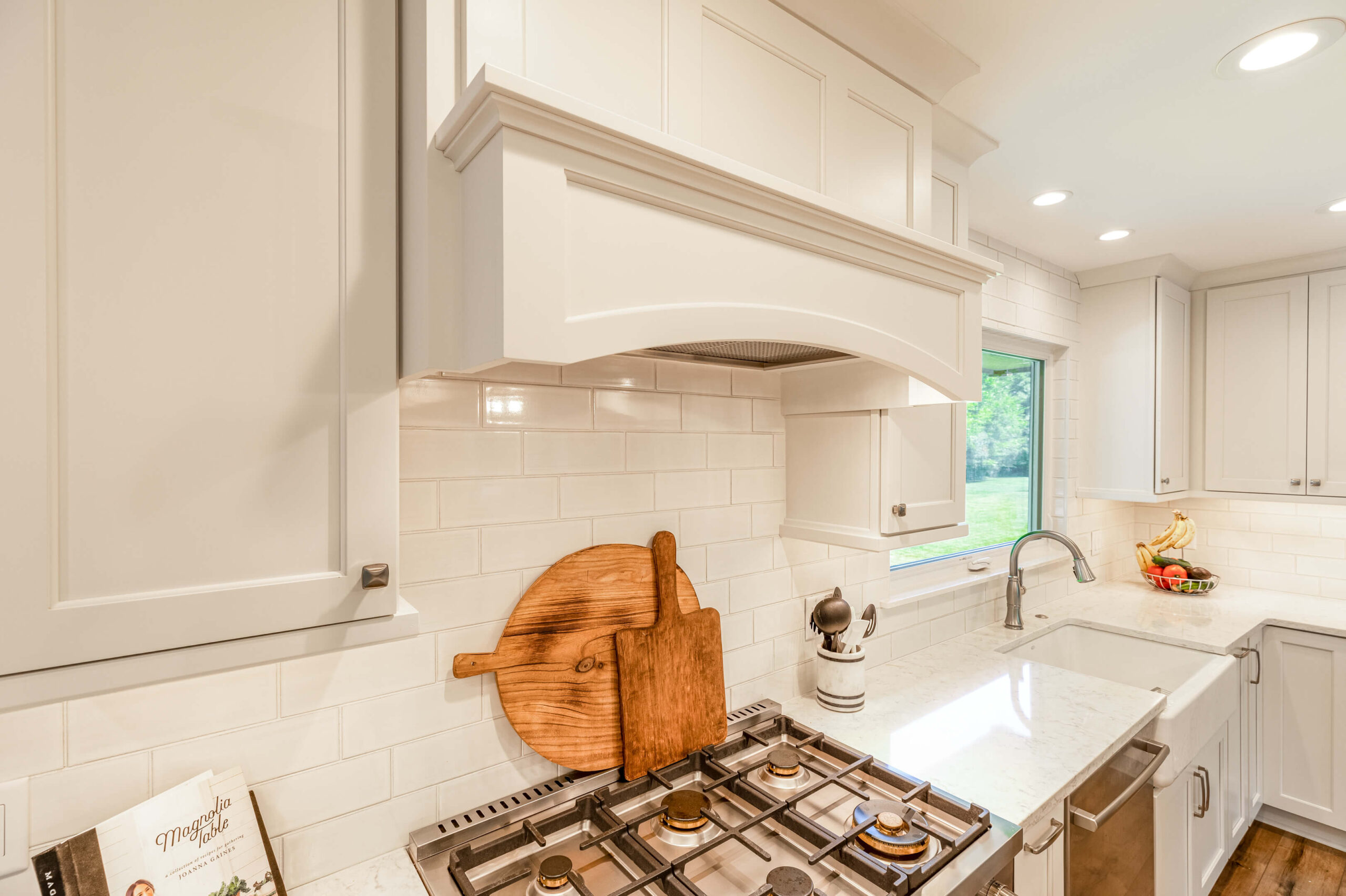 MJ Cabinet Designs' kitchen remodel with cherry cabinets, white center island with snack bar, and industrial lighting fixtures; dining table in foreground.